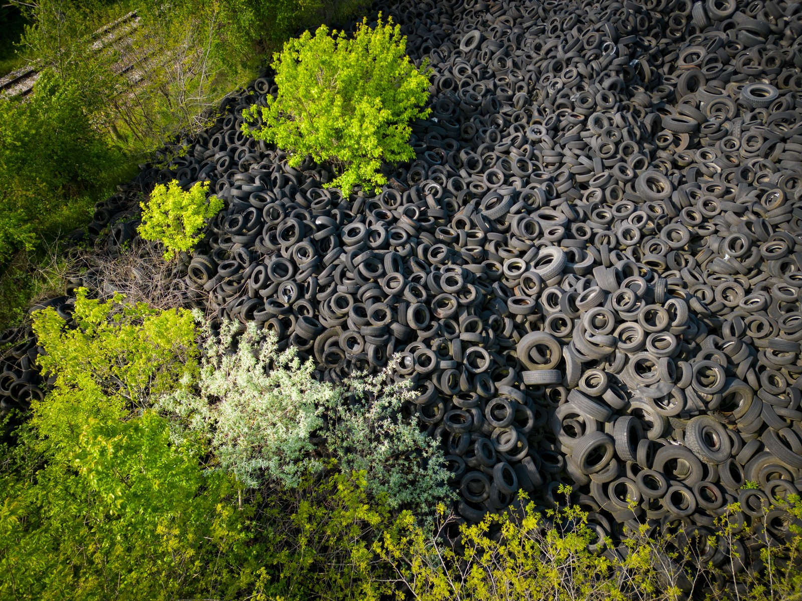 Aerial view of the stark contrast between a massive landfill of used car tires and the surrounding green trees. Tire dump showcases human waste impact on environment